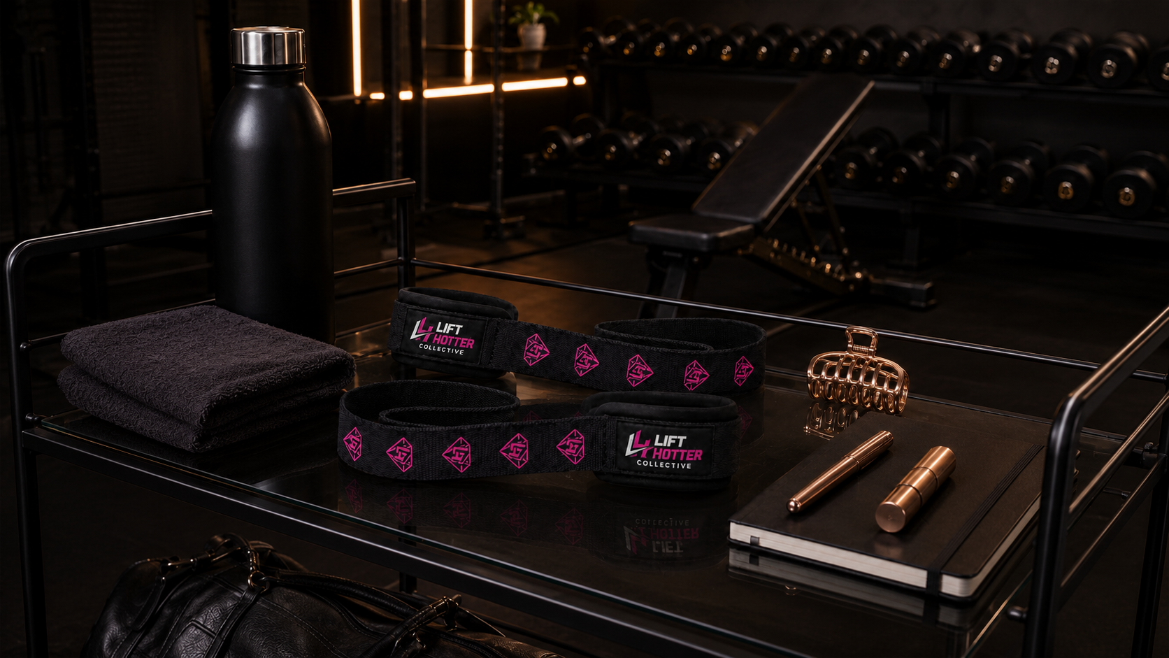 Lift Hotter lifting straps styled on a bar cart with water bottle, hair clip, and notebook in a home gym